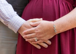 Close-up view of hands wearing wedding rings against a burgundy dress background.