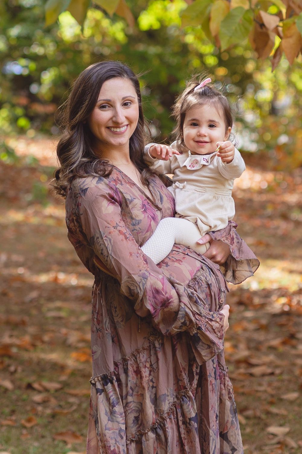 Mother and child in matching mauve dresses share joyful moments among autumn leaves in an outdoor photoshoot.