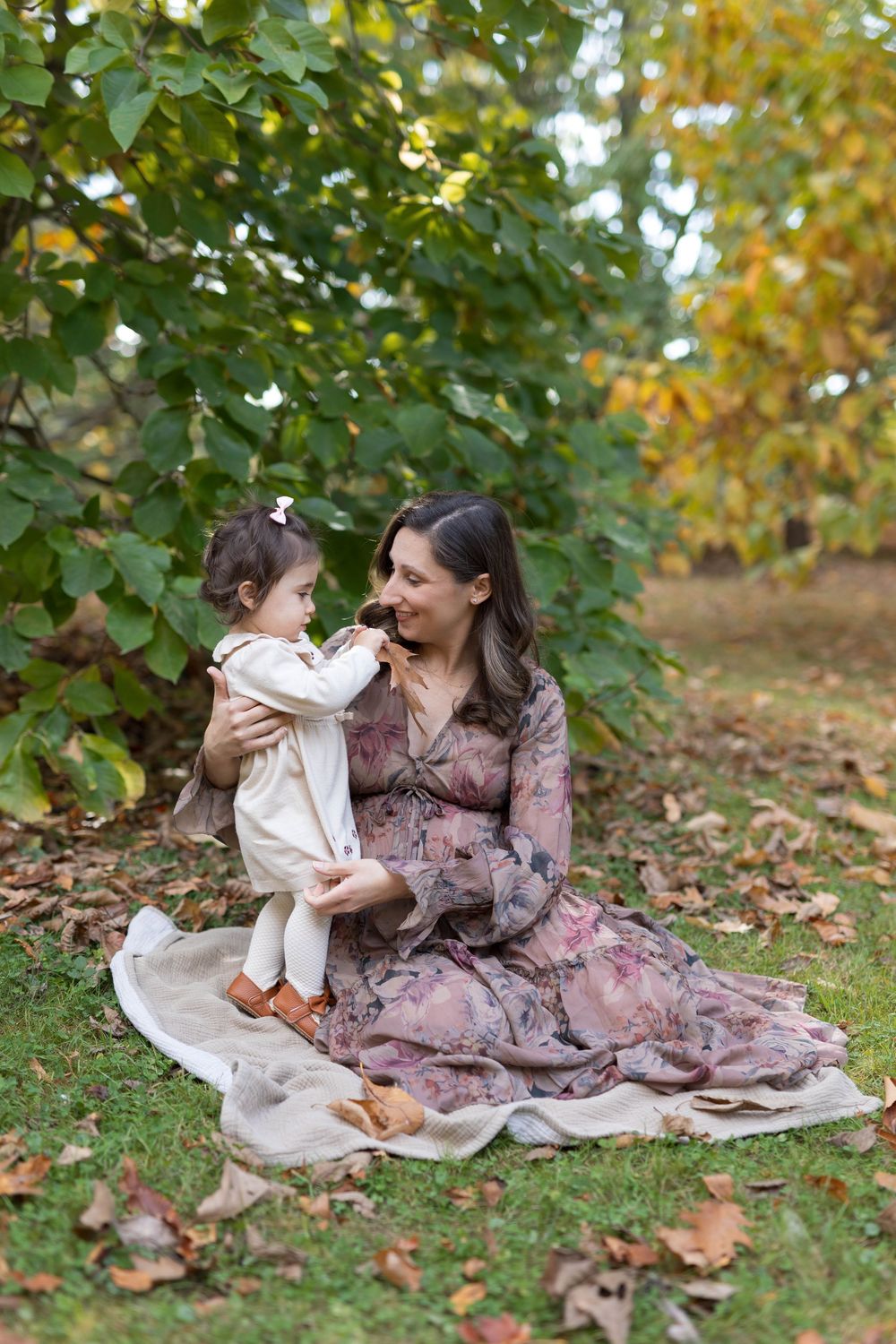 Family enjoying autumn day together on blanket spread over fallen leaves.