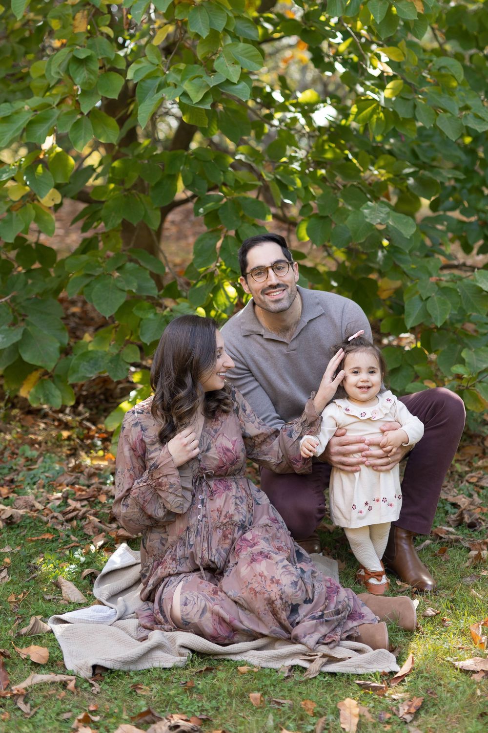 A family sits together on a blanket under autumn trees enjoying a tender moment in coordinated brown outfits.