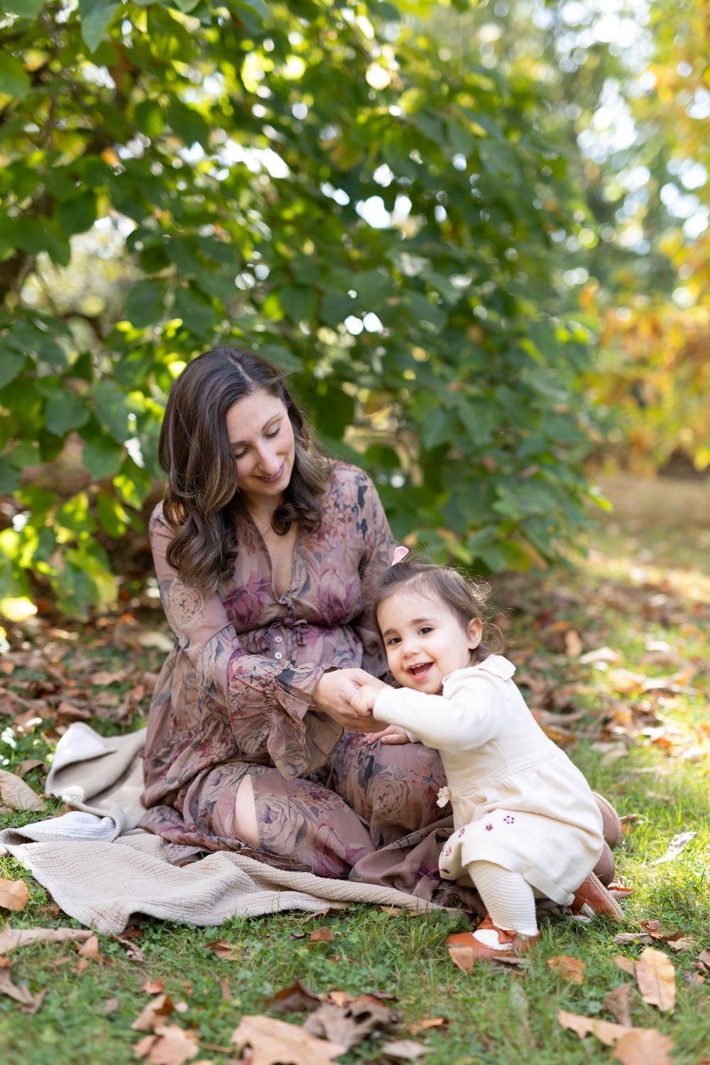 A tender moment captured on a blanket in autumn leaves as a floral dress-clad pair share cuddles outdoors.