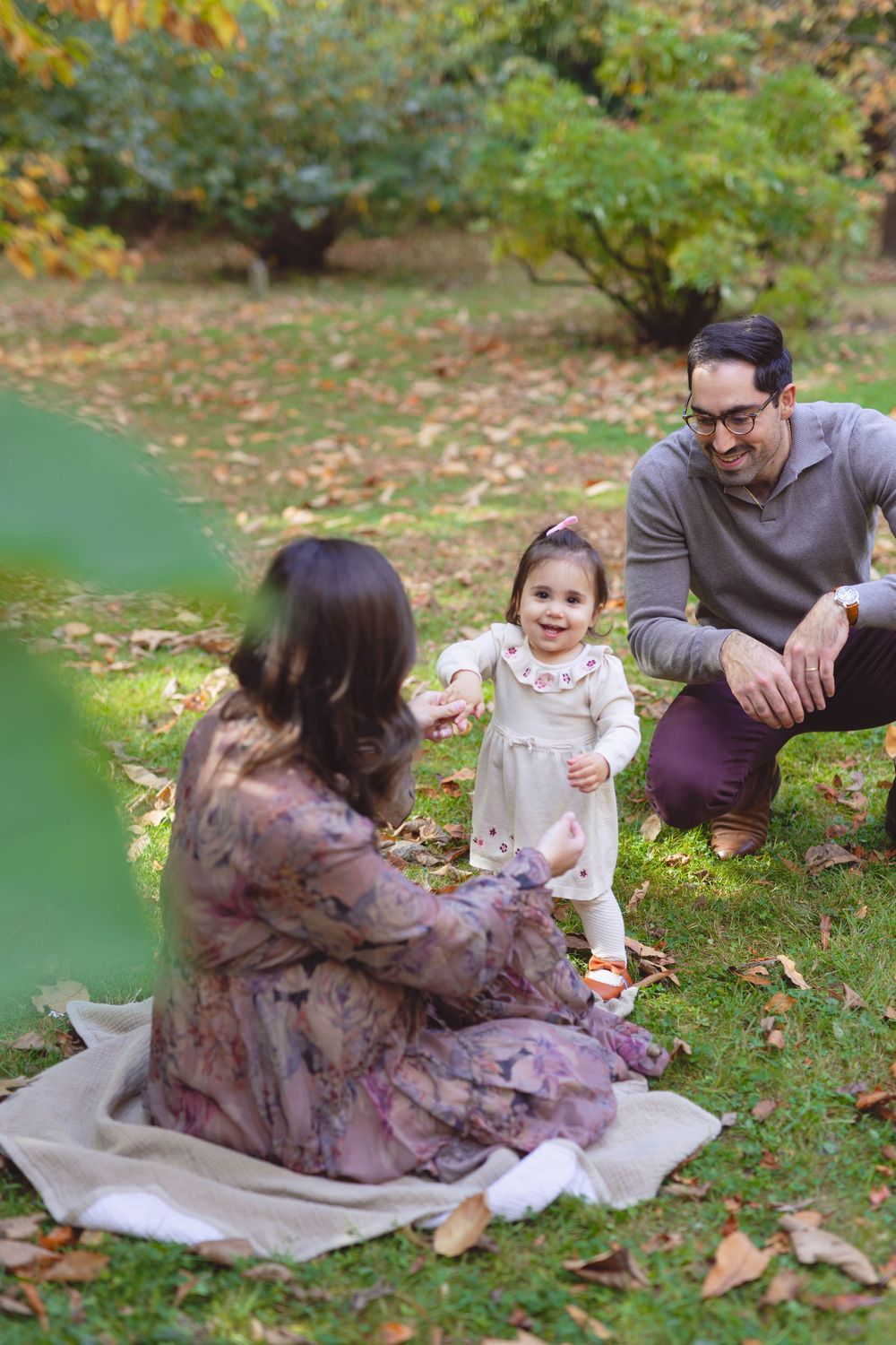 A family enjoying a fall day together on a blanket in a park with autumn leaves scattered on the ground.