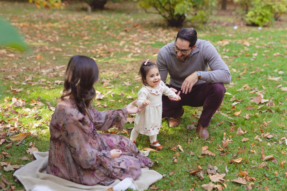 A family enjoys a picnic together on fallen autumn leaves in a park setting.