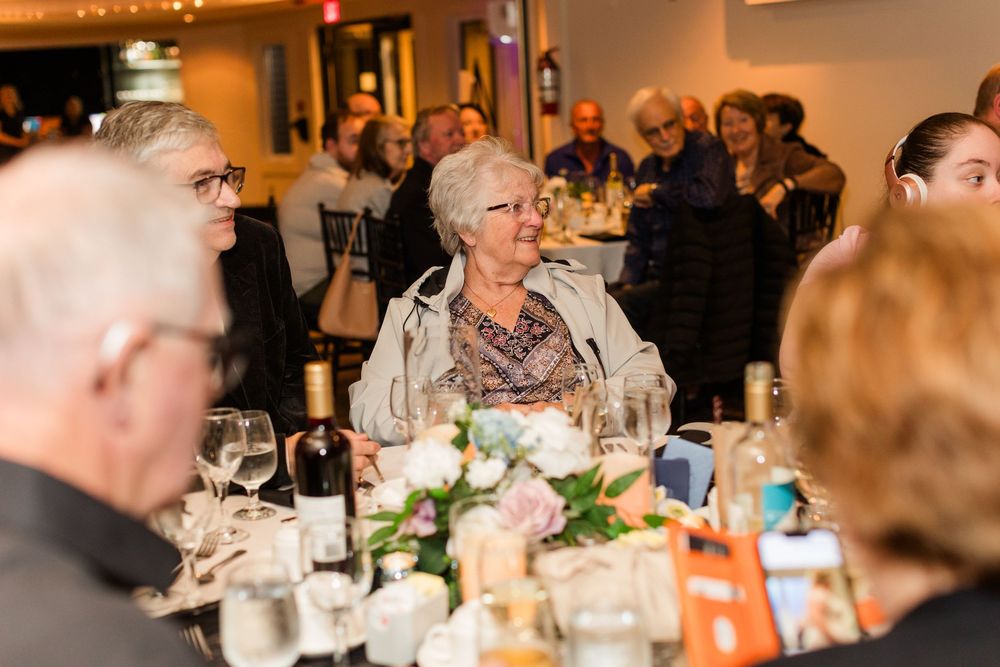 Guests seated at round tables during an elegant indoor banquet or reception with warm lighting and floral centerpieces.