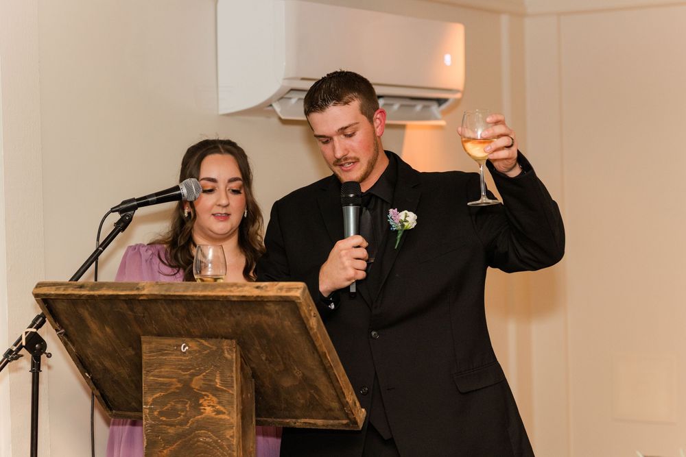 Wedding guests laugh and smile while seated at decorated reception tables with twinkle lights in background.