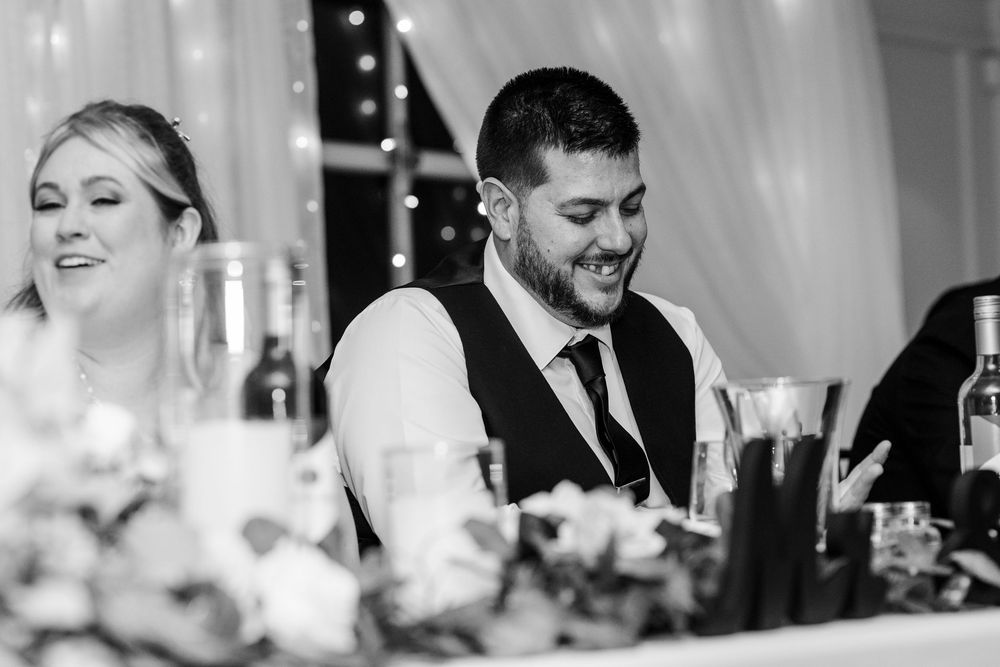 A joyful couple and their wedding guests laugh together during an elegant reception celebration.