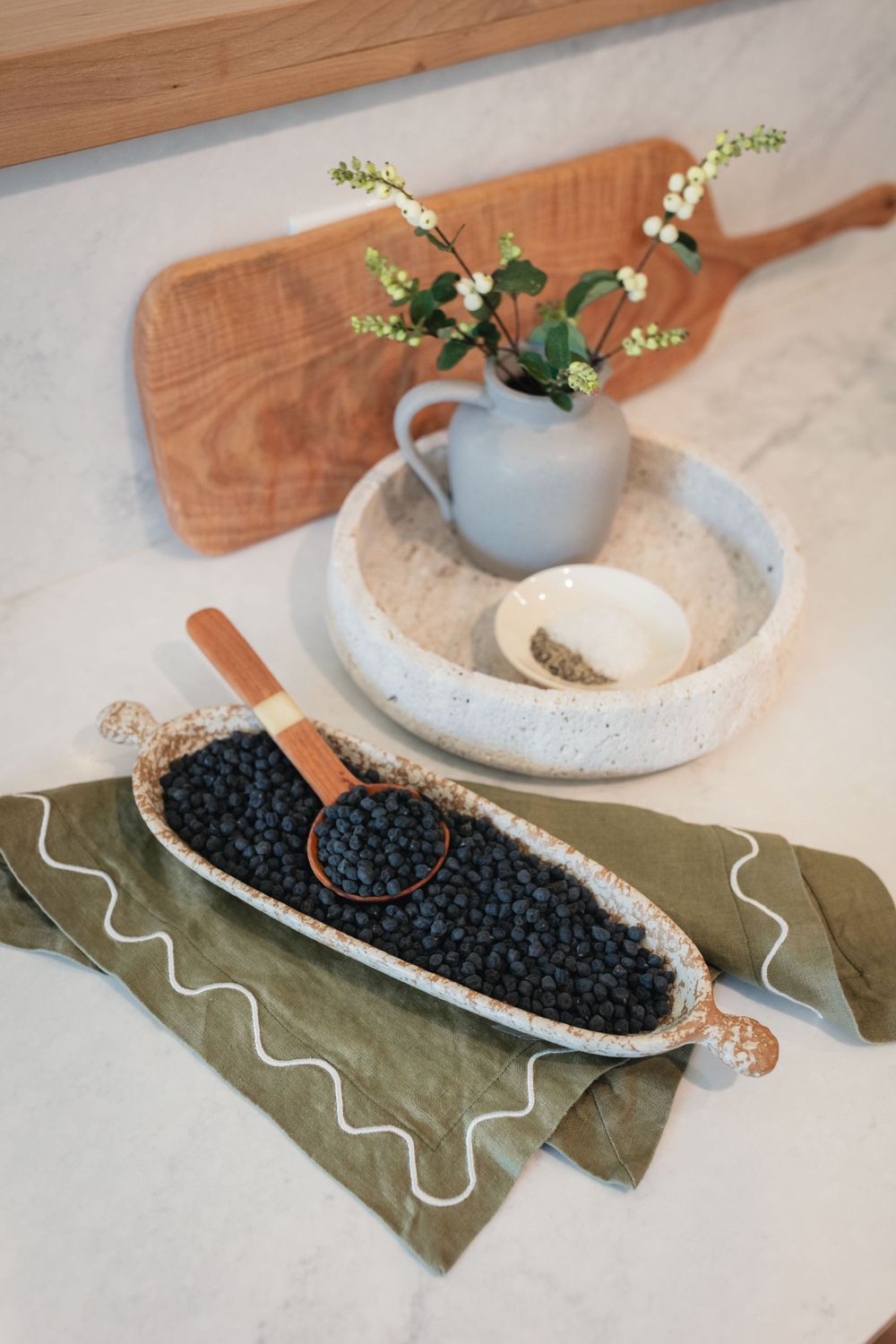 Rustic table setting with bowl of blueberries, ceramic vase with flowers, and green linen napkin.