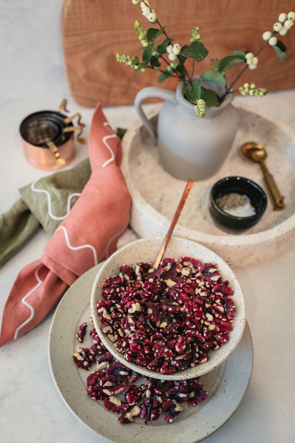 Artistic table setting with pomegranate seeds, coral napkins, and small floral arrangement.