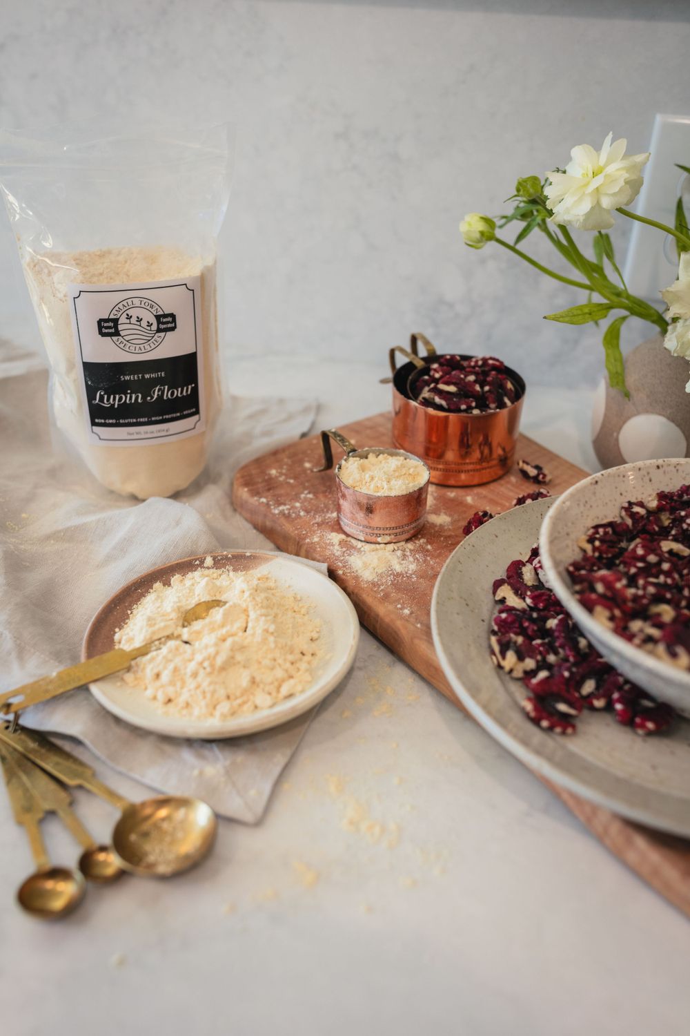 Baking ingredients and pomegranate seeds arranged on light surface with flour bag and measuring spoons.