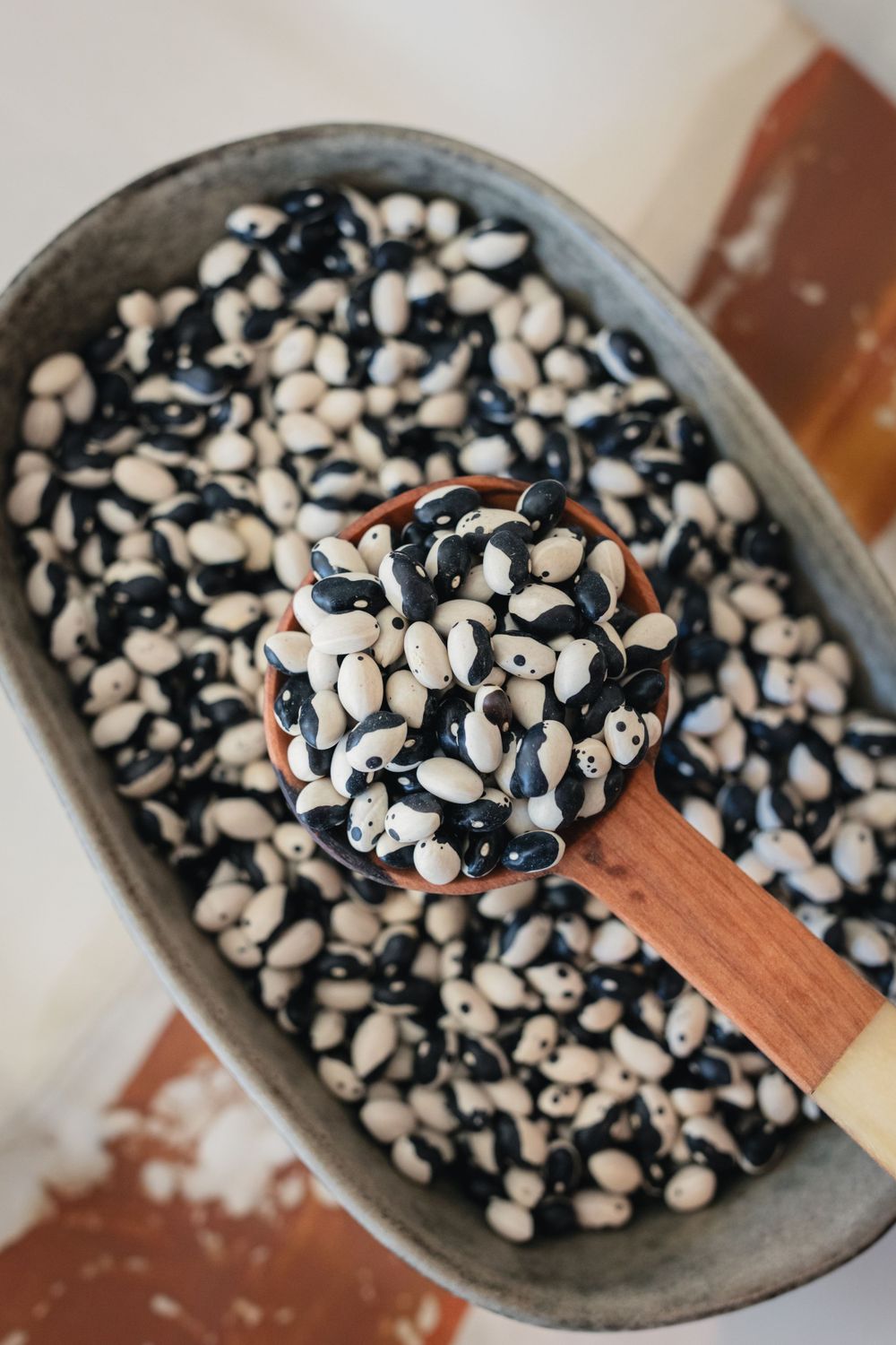 Mixed black and white beans in gray ceramic bowl with wooden spoon.
