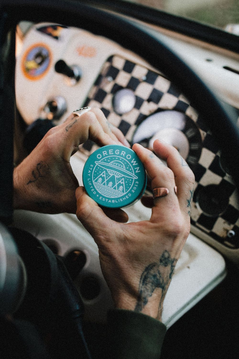 Teal branded container held inside vehicle with checkered dashboard pattern.