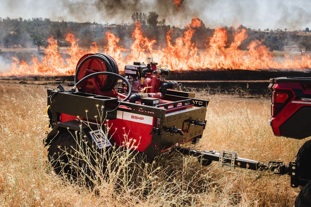 Fire suppression equipment mounted on a red vehicle with flames burning in the background.