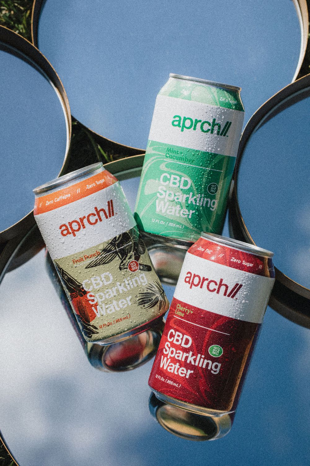 Three cans of Aprch CBD sparkling water in different flavors reflected in mirrors.