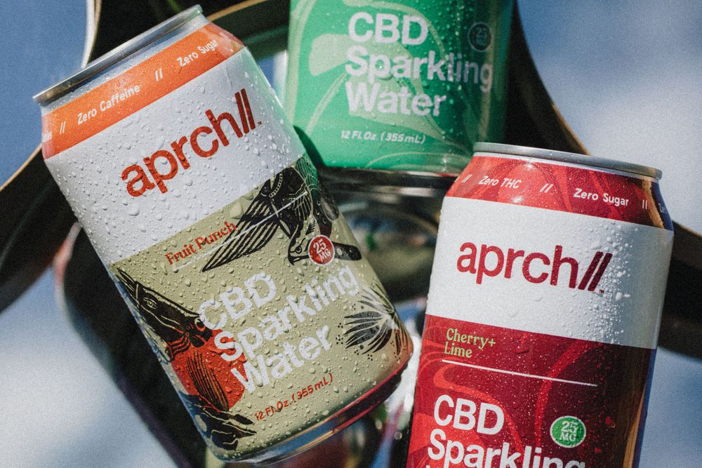 Multiple cans of Aprch CBD sparkling water drinks displayed on reflective surface.