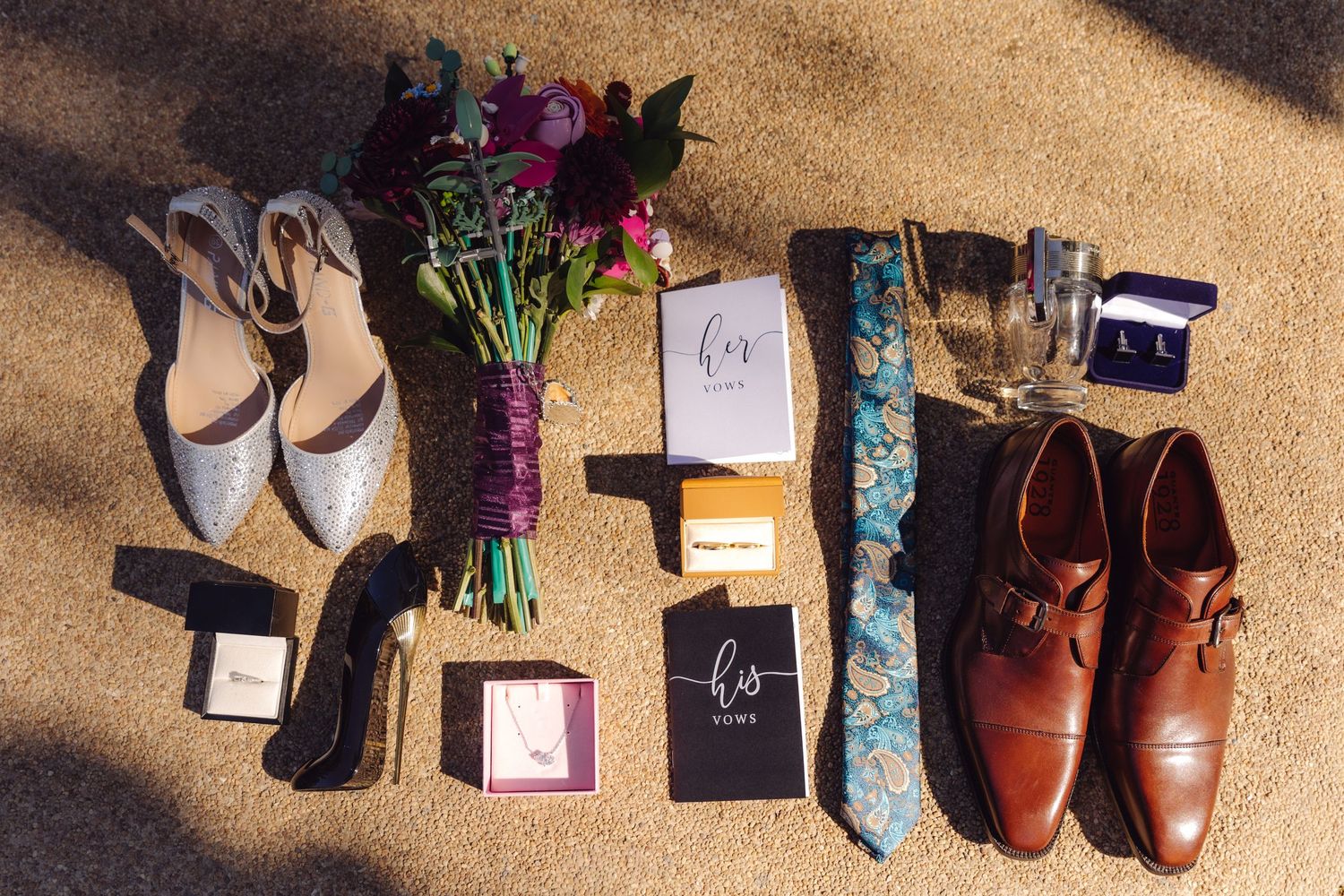 Flat lay of wedding accessories including bouquet, shoes, ties, rings, and leather dress shoes.