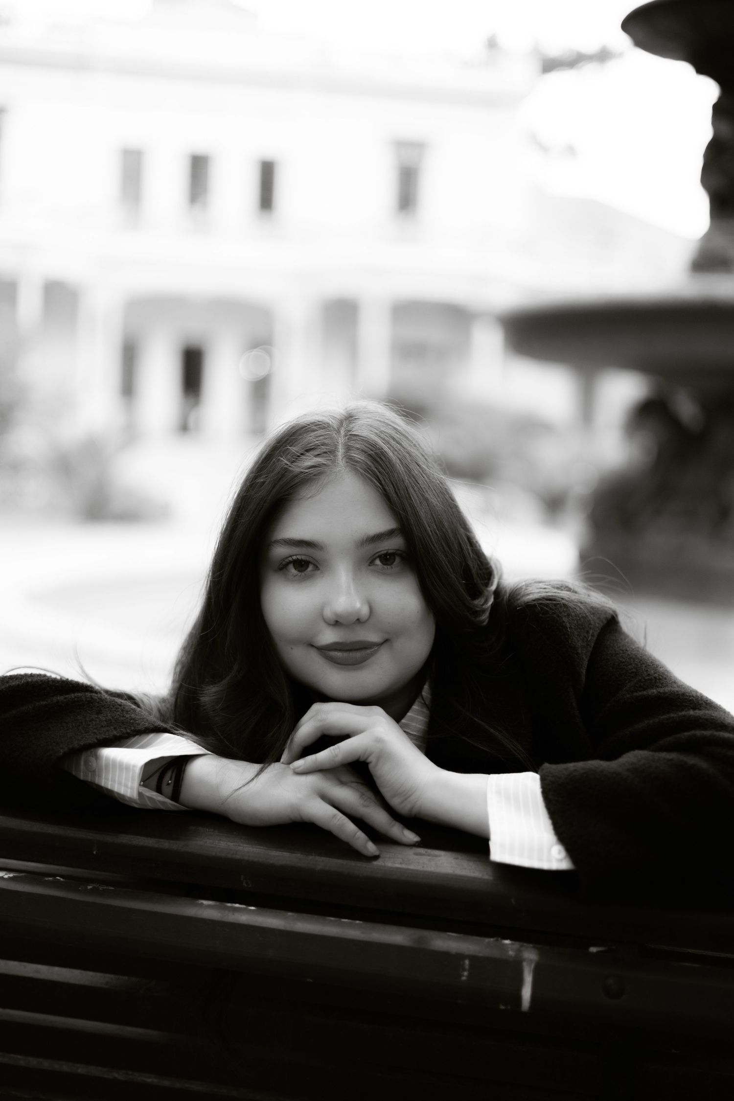 Black and white portrait of young woman resting chin on hands on park bench.
