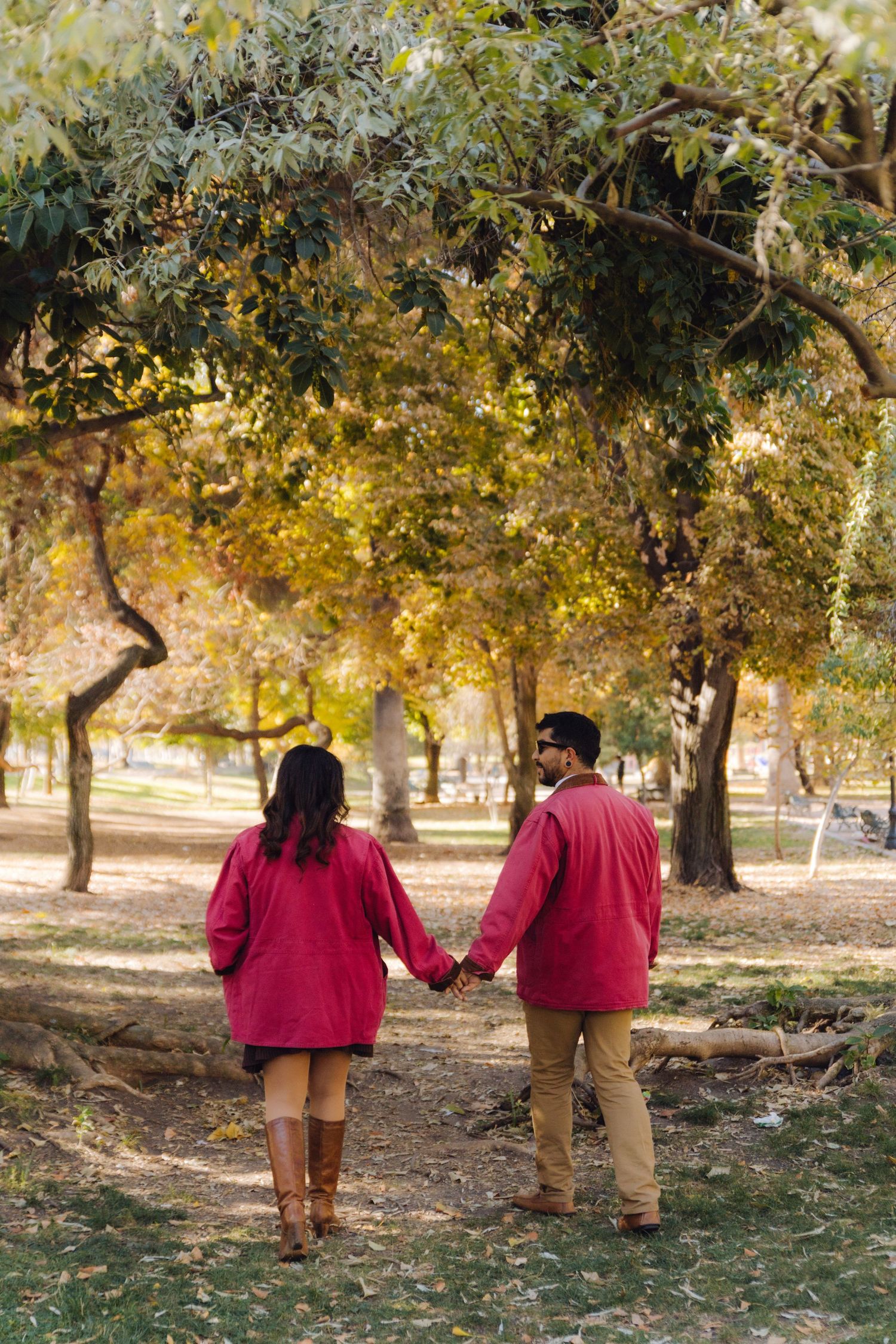 Couple in matching red jackets holding hands while walking through autumn park trees.