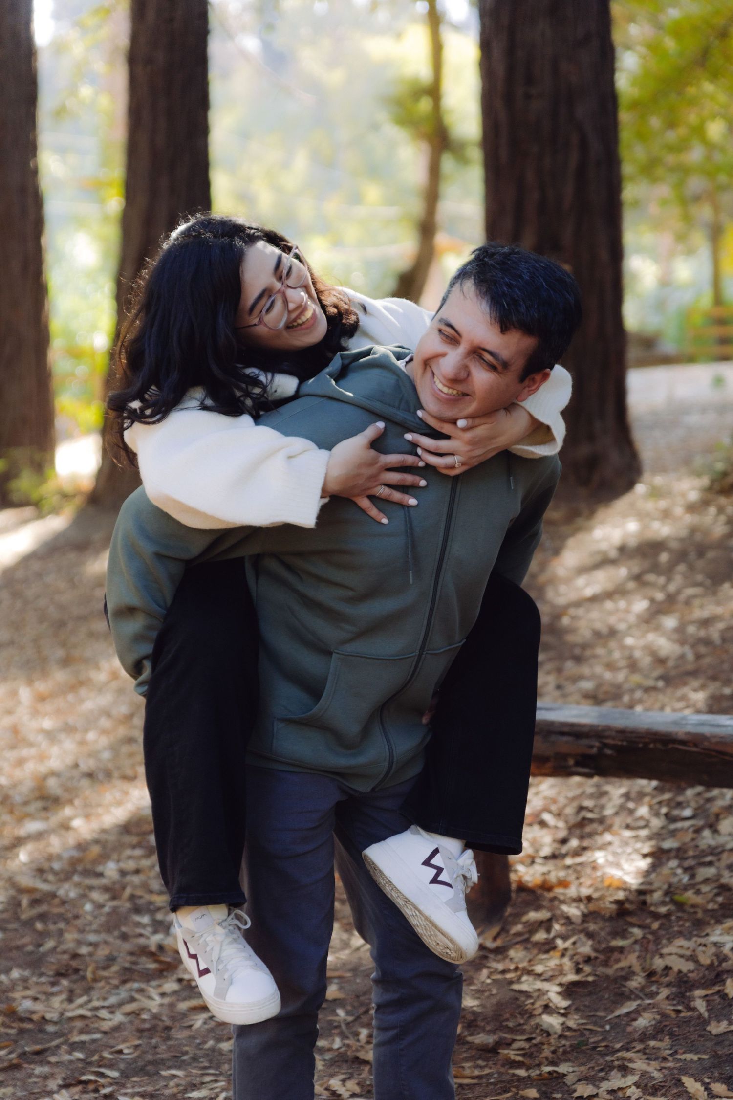 Smiling man giving a joyful woman a piggyback ride along a sunlit forest path in autumn.
