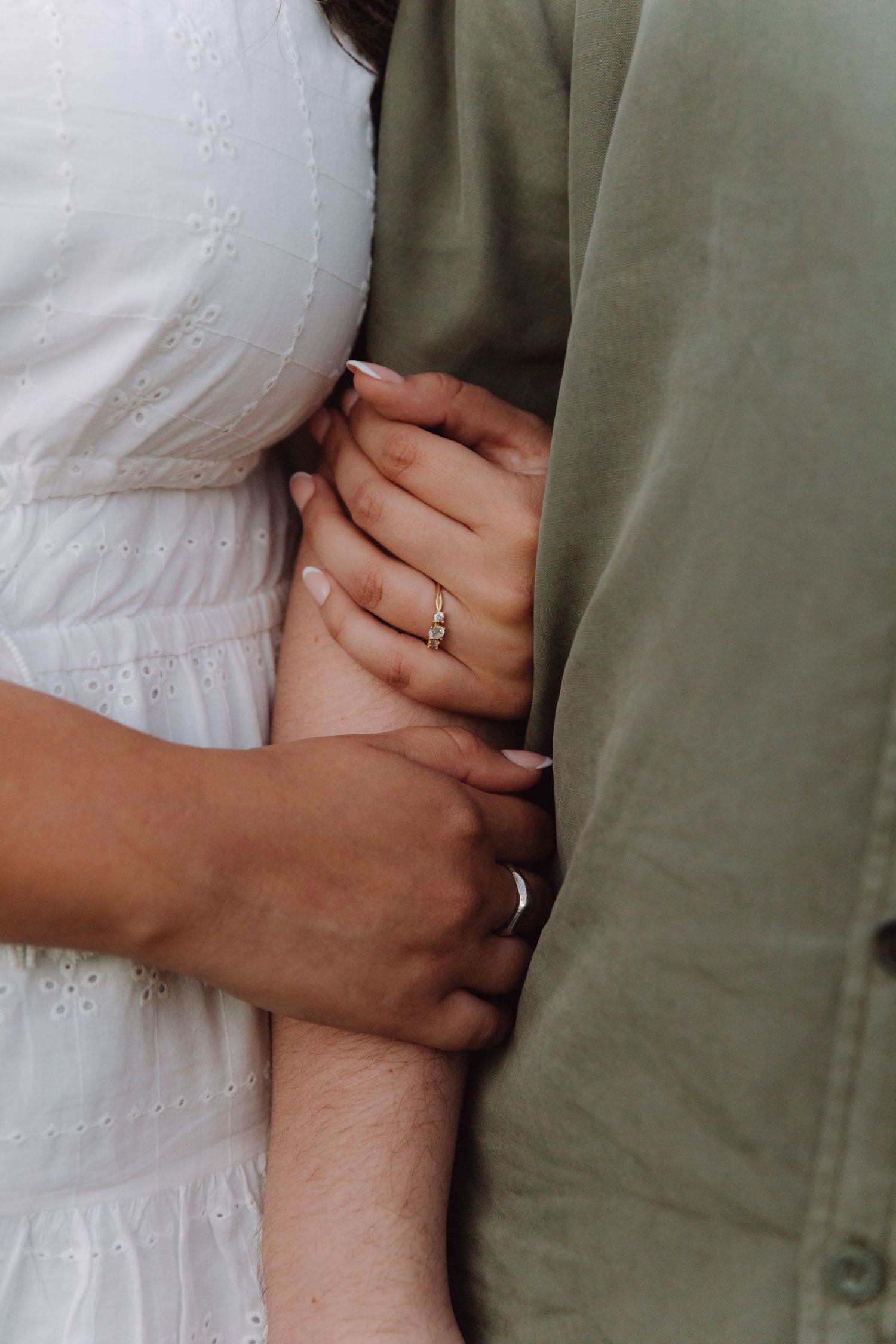 Close-up of couple holding hands, bride wearing elegant diamond engagement ring in white dress.