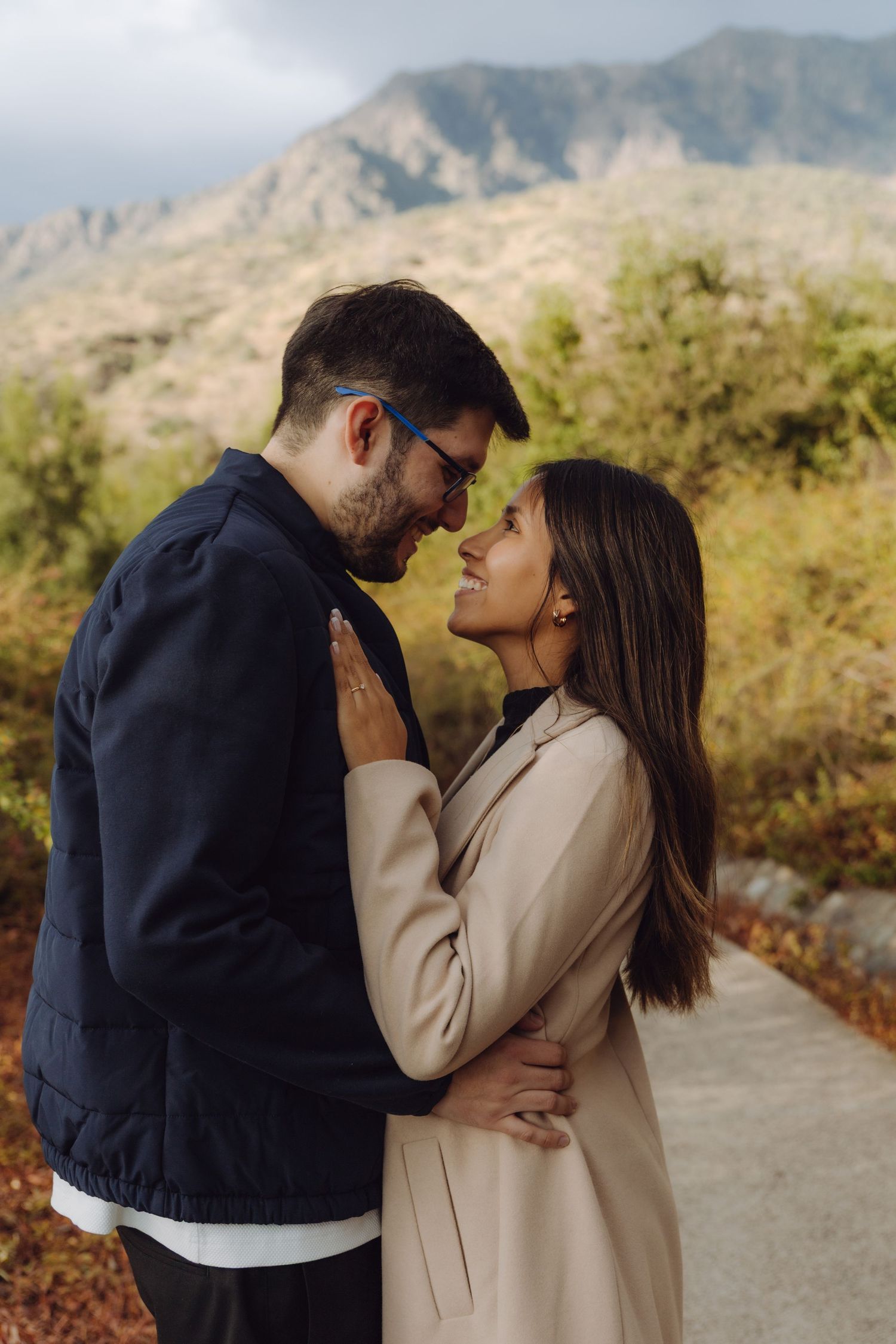 Romantic couple embracing and smiling at each other with mountain landscape in background.