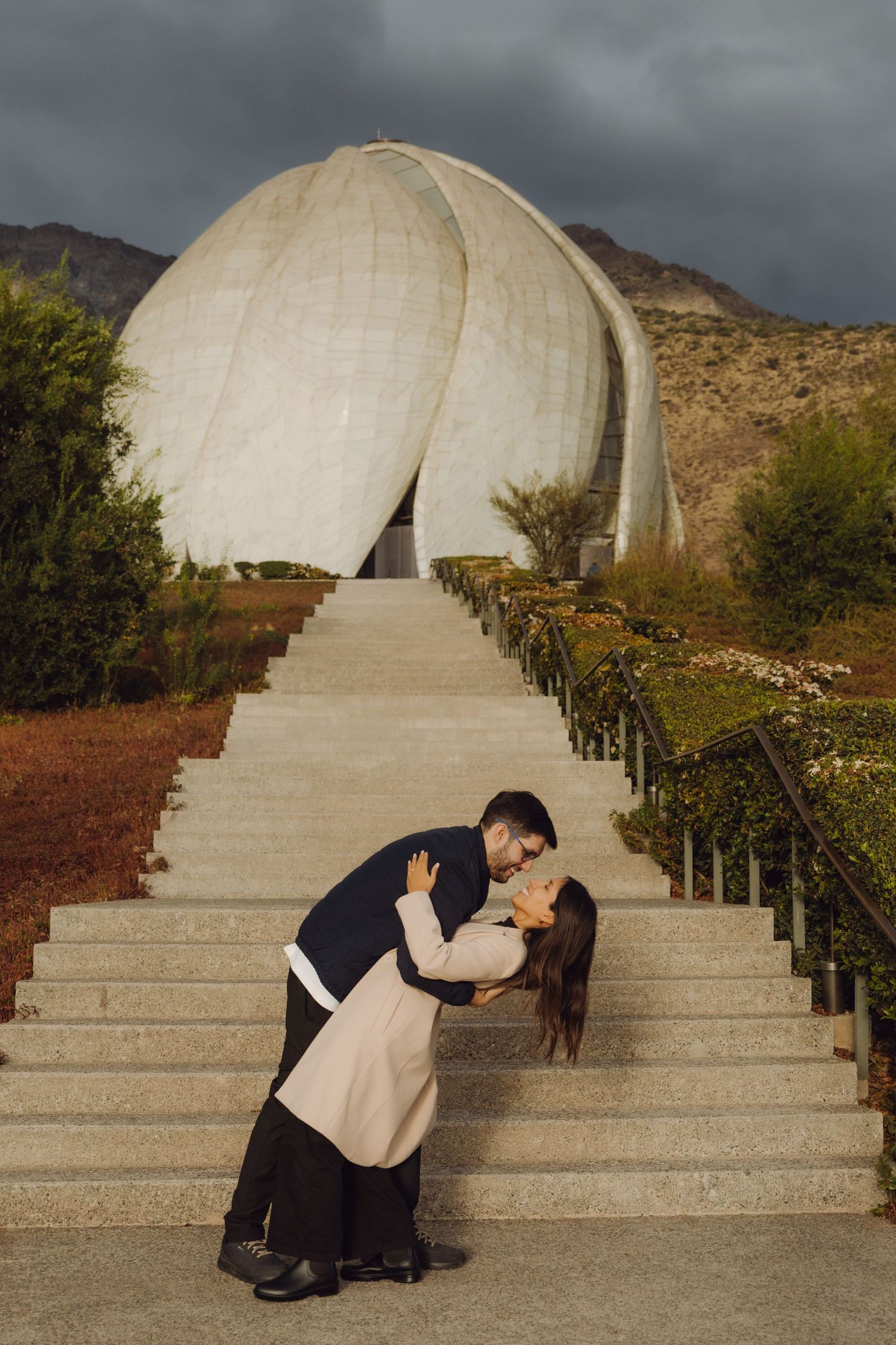 Couple sharing a dip kiss on steps in front of a large white lotus-shaped temple.
