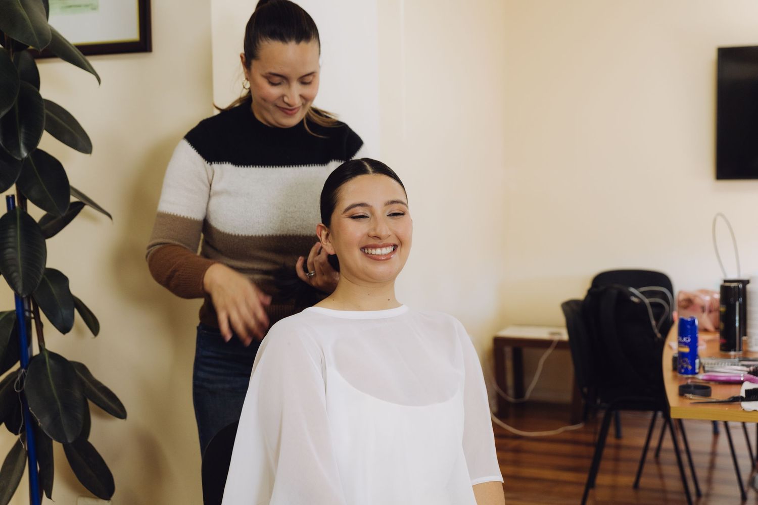 Hairstylist styling smiling bride's hair in a bright salon before wedding ceremony.