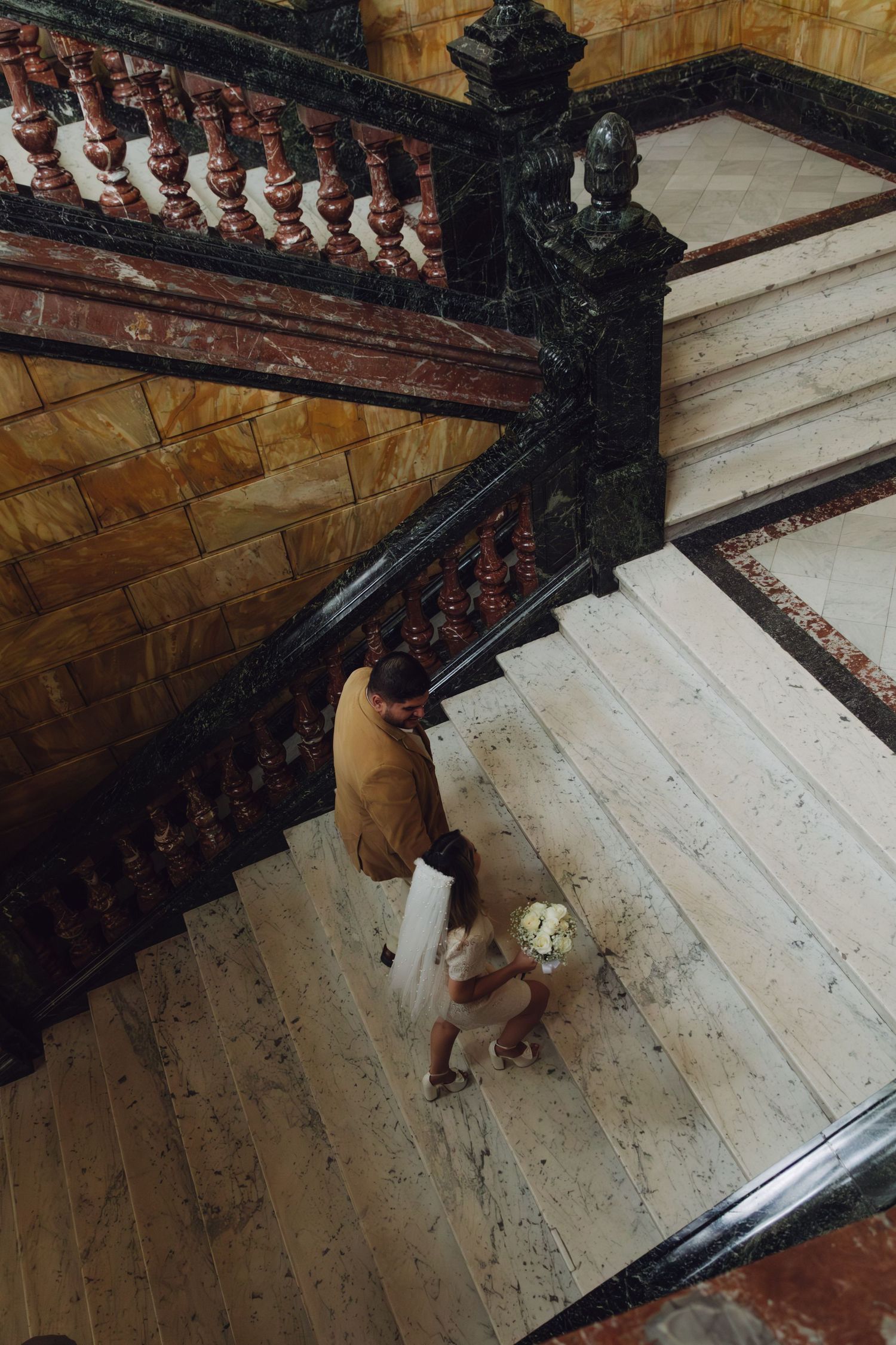 Aerial view of a couple walking down an ornate marble staircase in an elegant historic building.