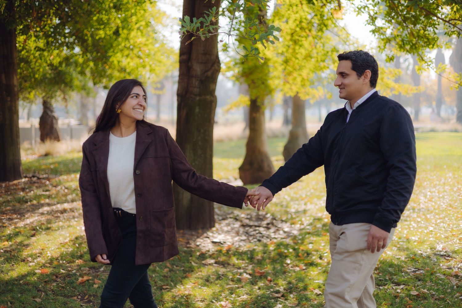 Joyful couple holding hands and walking through a sunny autumn park with golden foliage trees.
