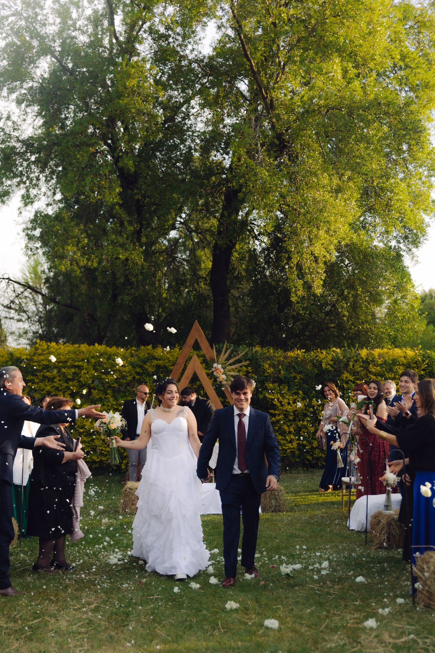 Bride and groom walking down the aisle as guests shower them with white petals at outdoor wedding.