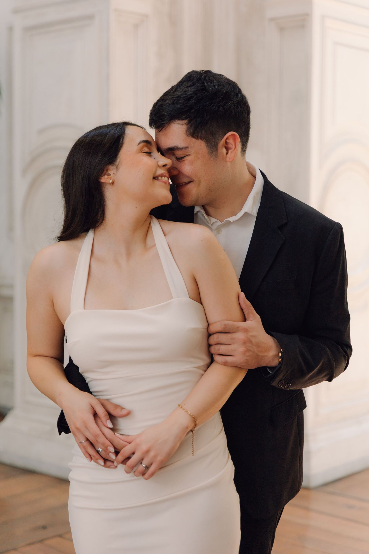 Romantic couple embracing and smiling together, bride in white halter dress and groom in black suit.