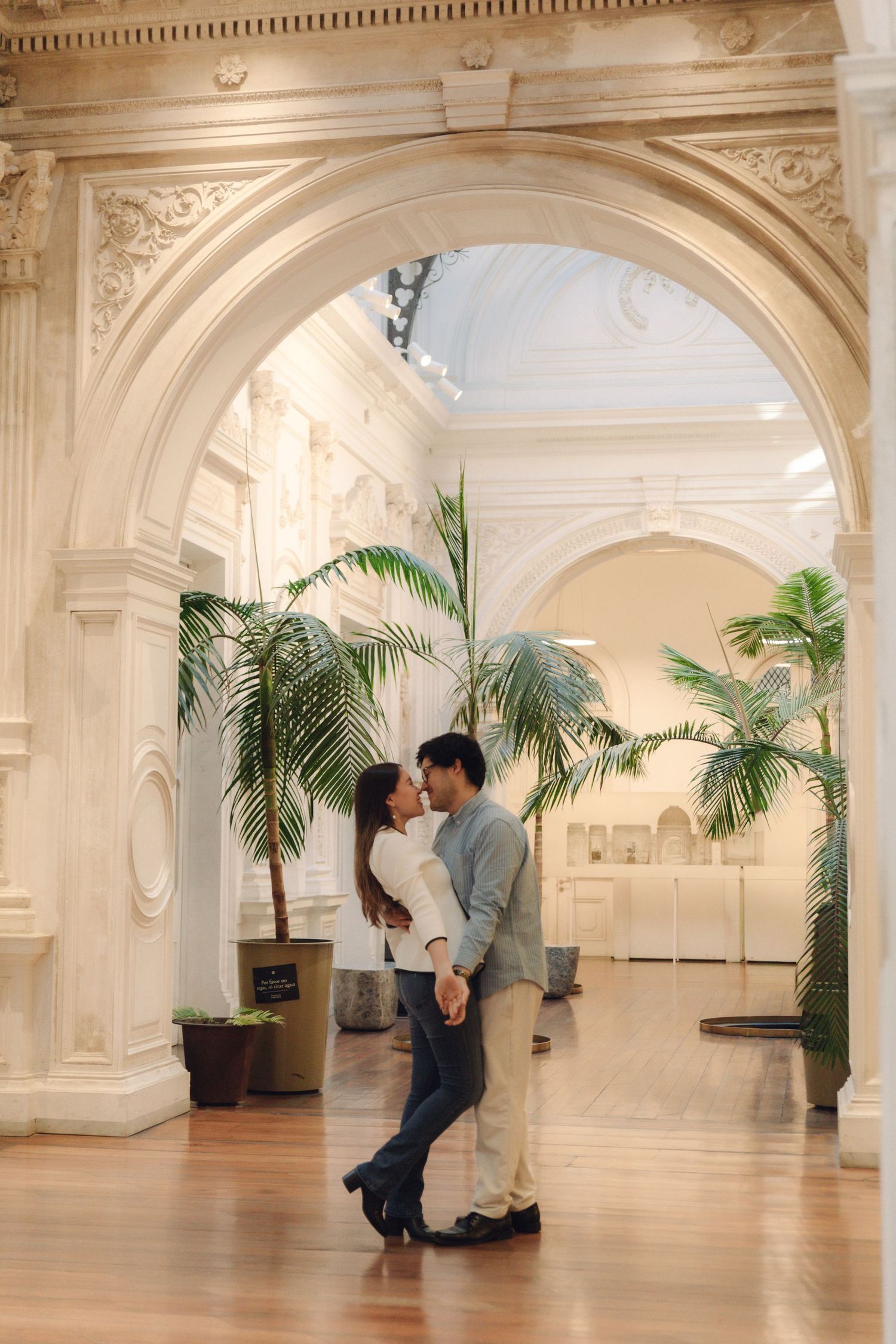 Romantic couple kissing under grand marble arch in elegant museum hall.