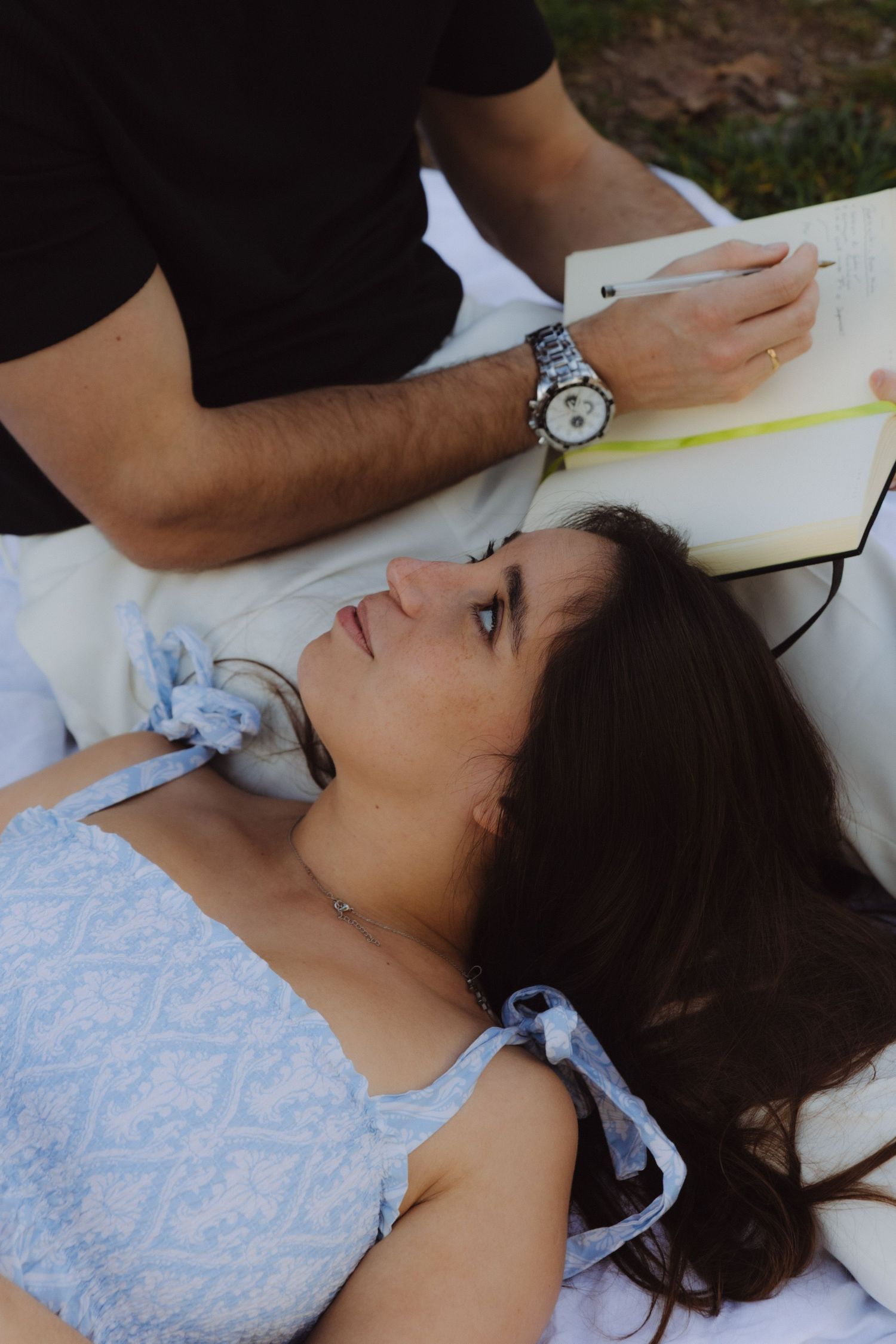 Woman lying down looking up at man writing in notebook outdoors.