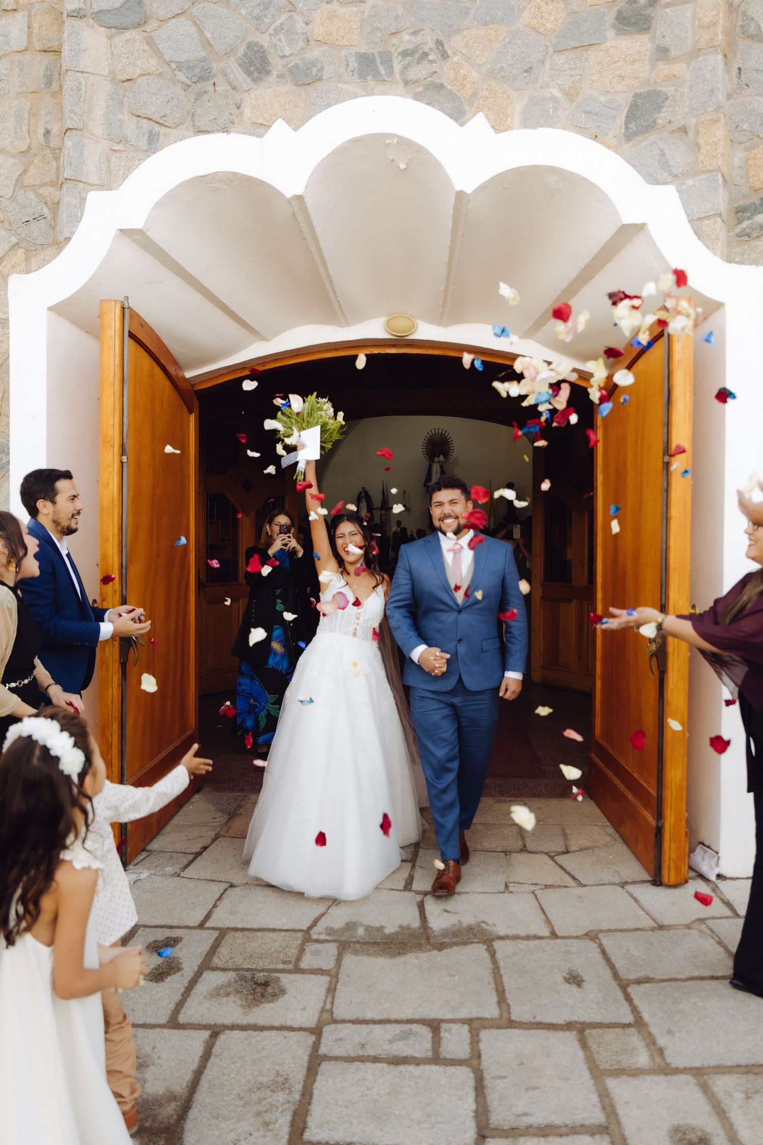 Newlyweds exit church doors as guests toss colorful confetti petals in celebration.