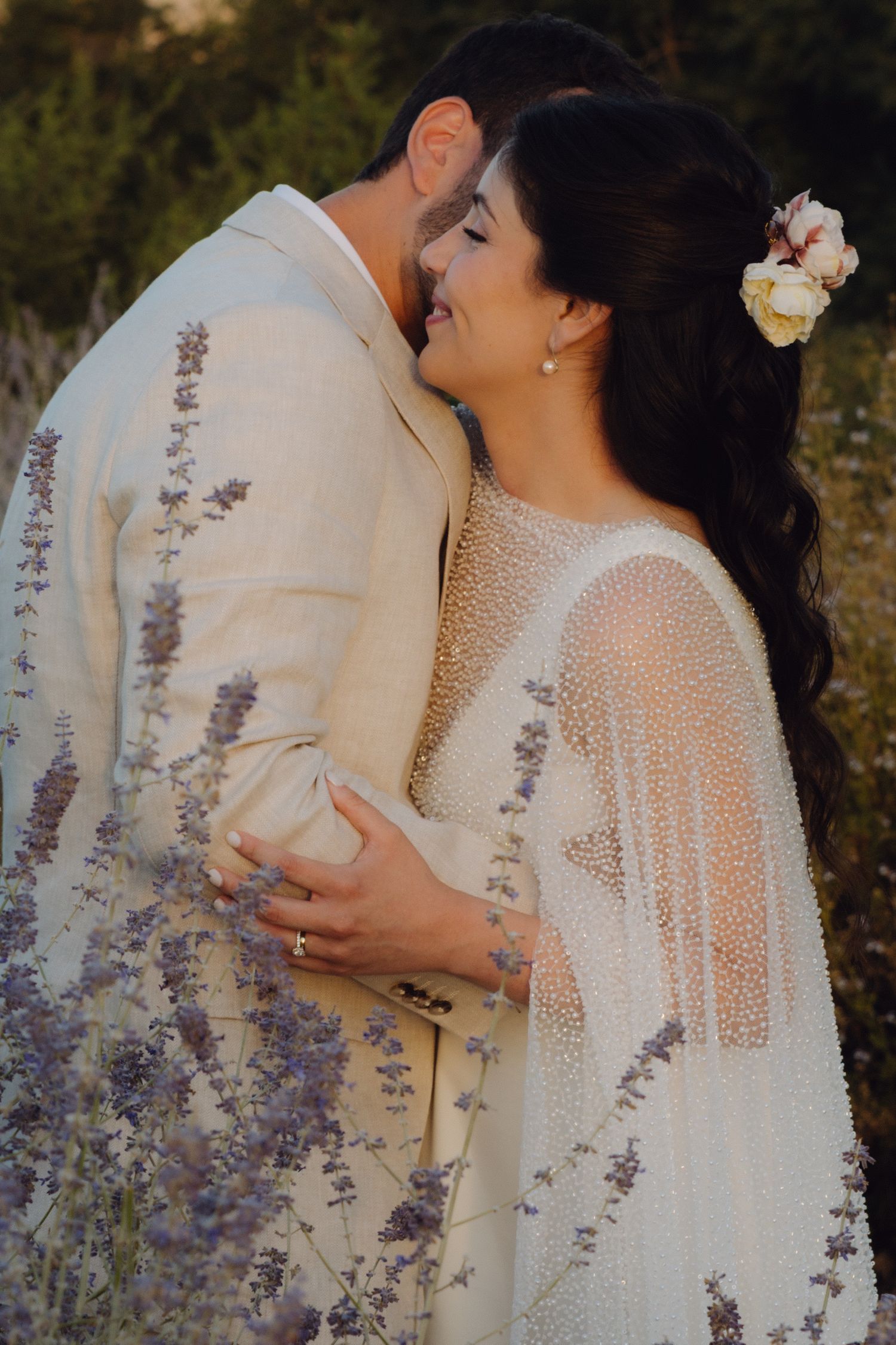 Bride and groom embrace romantically among lavender flowers at sunset in outdoor setting.