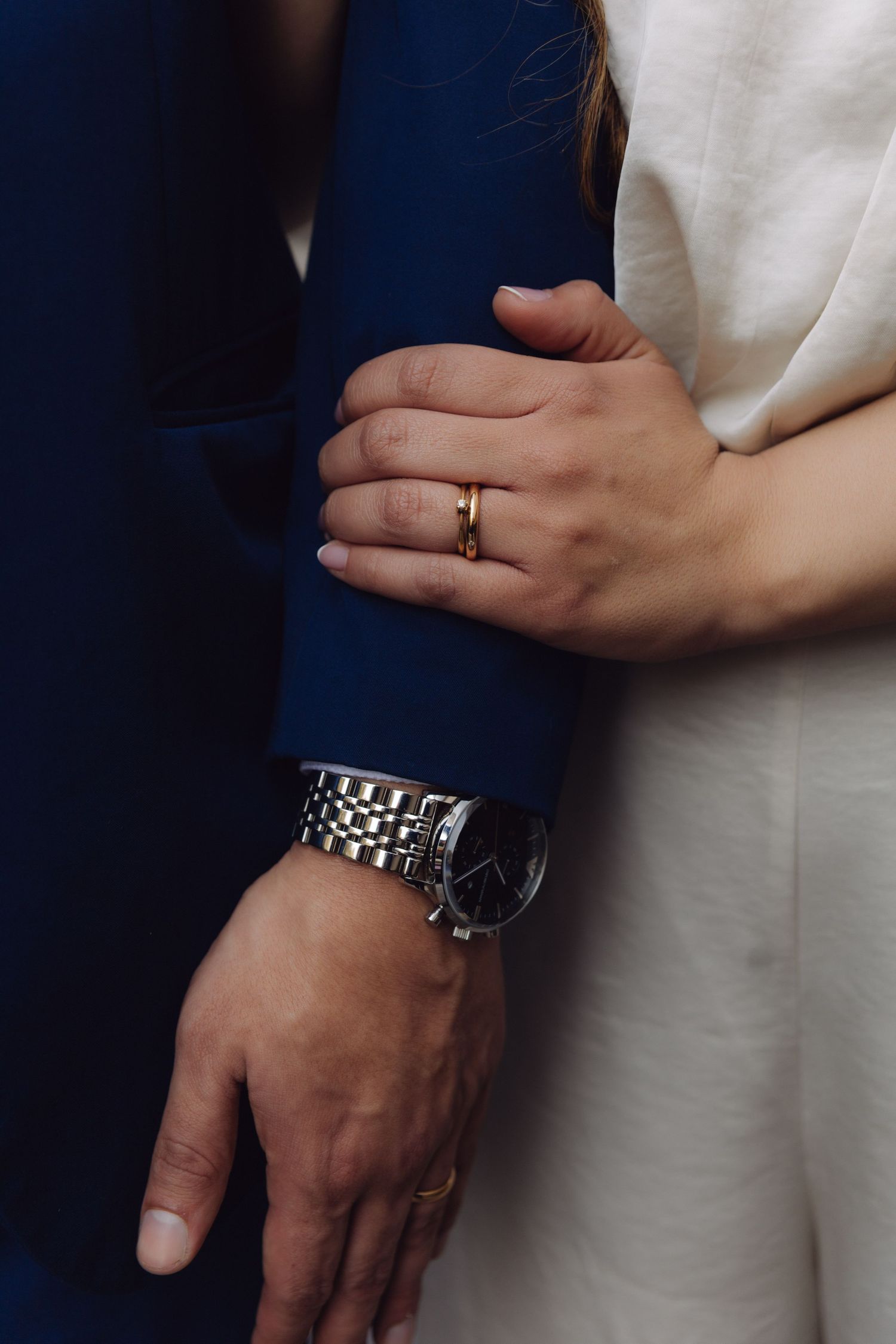 Close-up of bride and groom hands, featuring a gold wedding ring and silver watch.