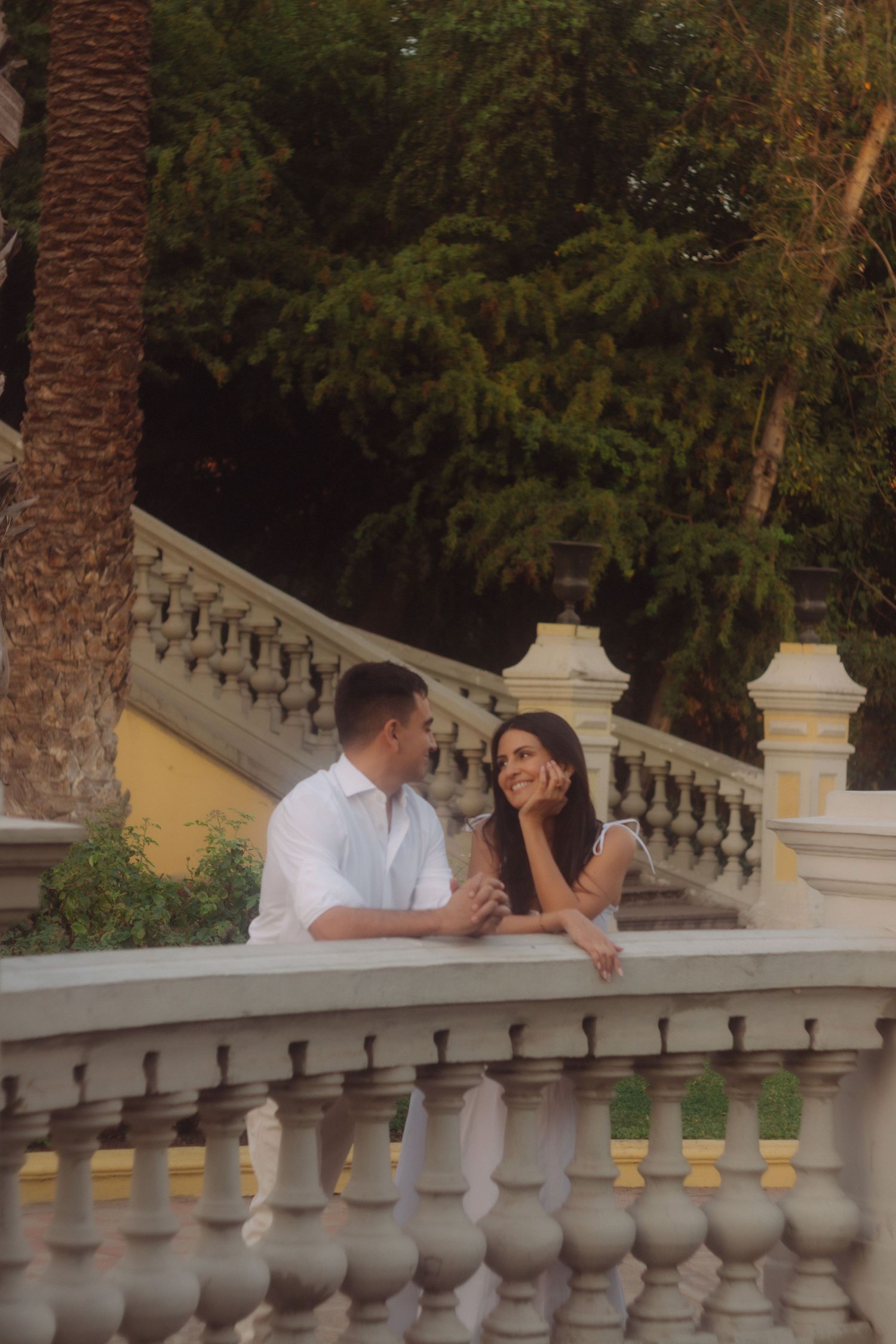 Romantic couple sharing an intimate moment on an elegant white balustrade staircase outdoors.