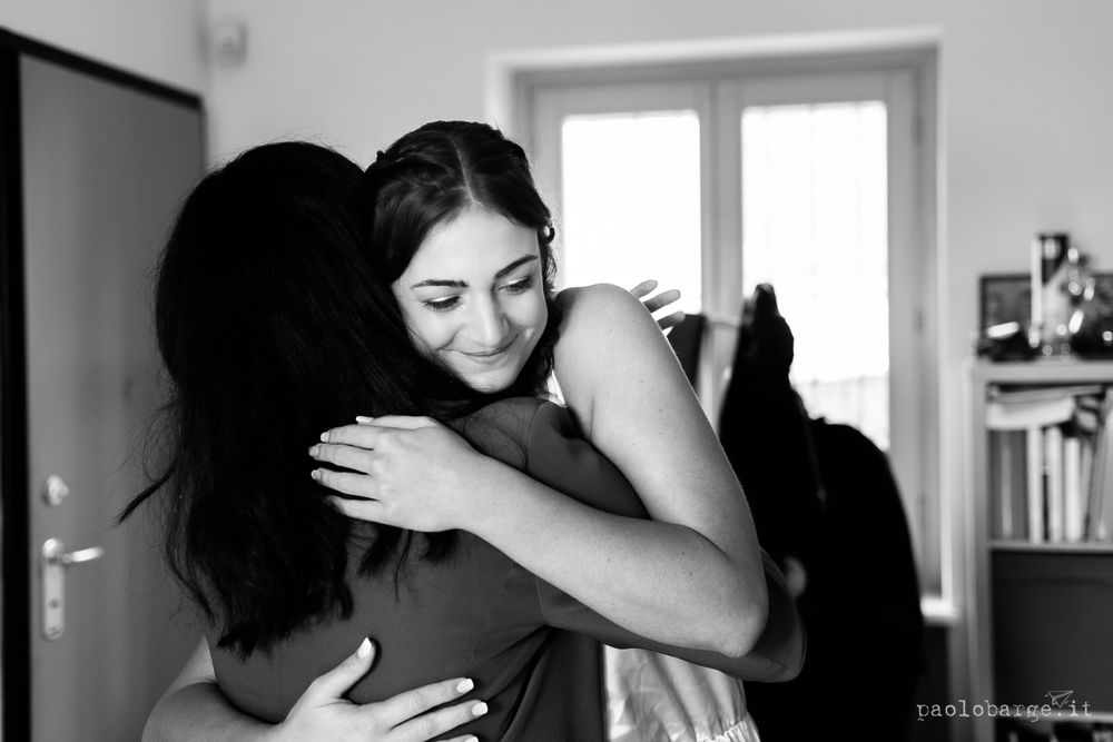 An emotional embrace captured in black and white photography during a wedding preparation moment.