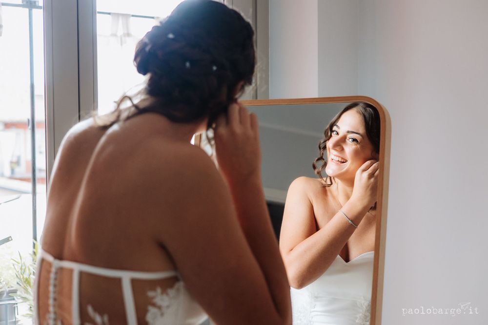 A person putting on earrings while looking in a mirror during wedding preparations.