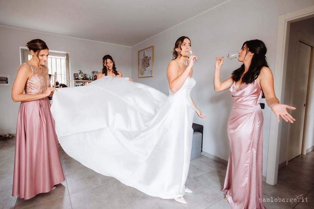 Bridesmaids in pink dresses help adjust a flowing white wedding gown during pre-ceremony preparations.