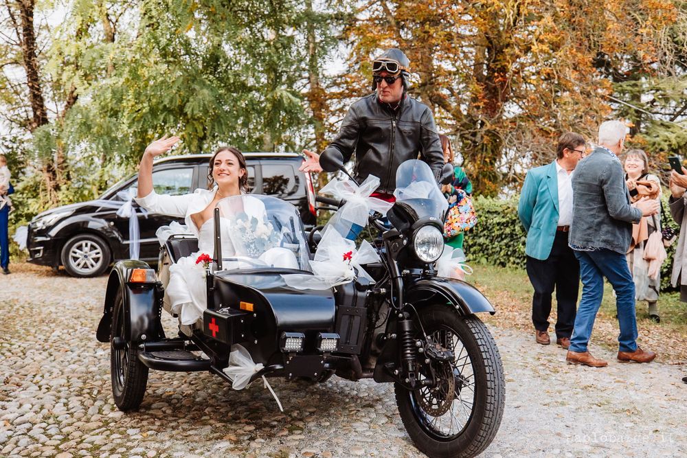 Newlyweds pose with vintage motorcycle and sidecar during autumn wedding celebrations.