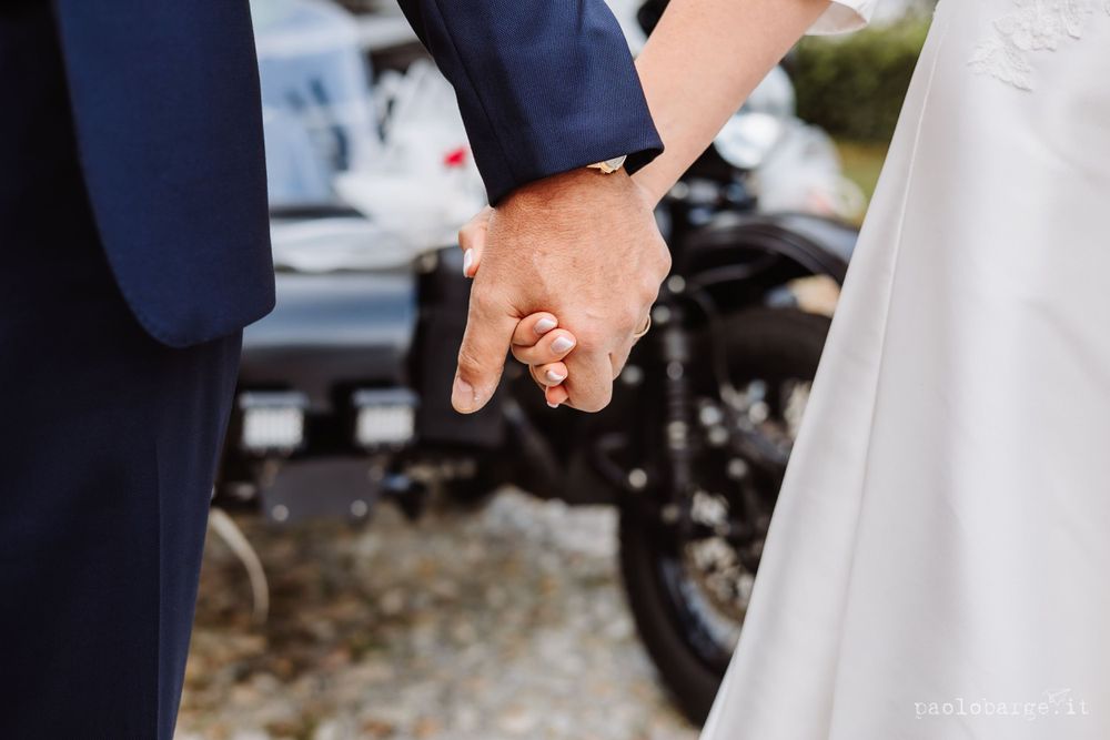Close-up of couple holding hands with motorcycle in background.