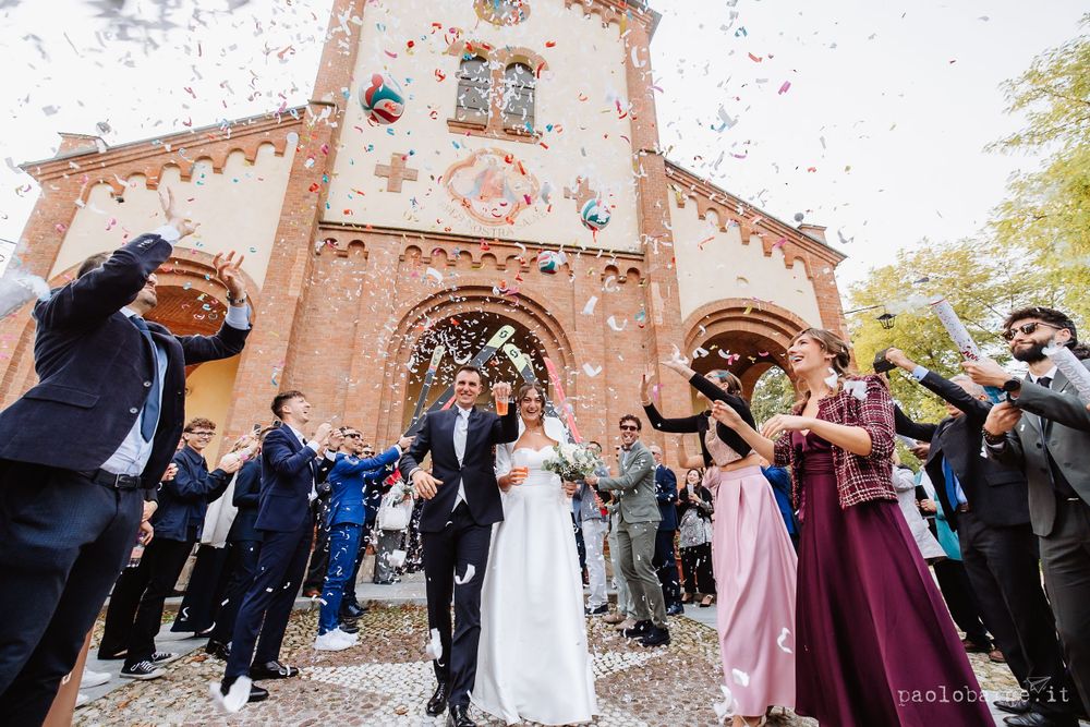 Wedding guests throw colorful confetti outside a historic brick church entrance.