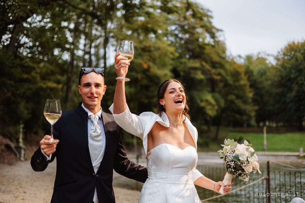 Wedding couple celebrates with champagne glasses outdoors amidst joyful laughter.