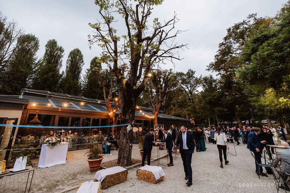 Guests mingle at an outdoor wedding reception venue with string lights and tall trees.