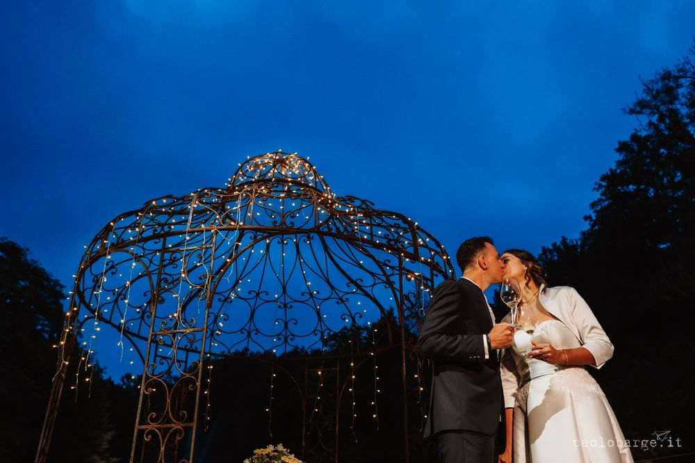 A romantic evening wedding ceremony under an illuminated metal gazebo against a dark blue sky.