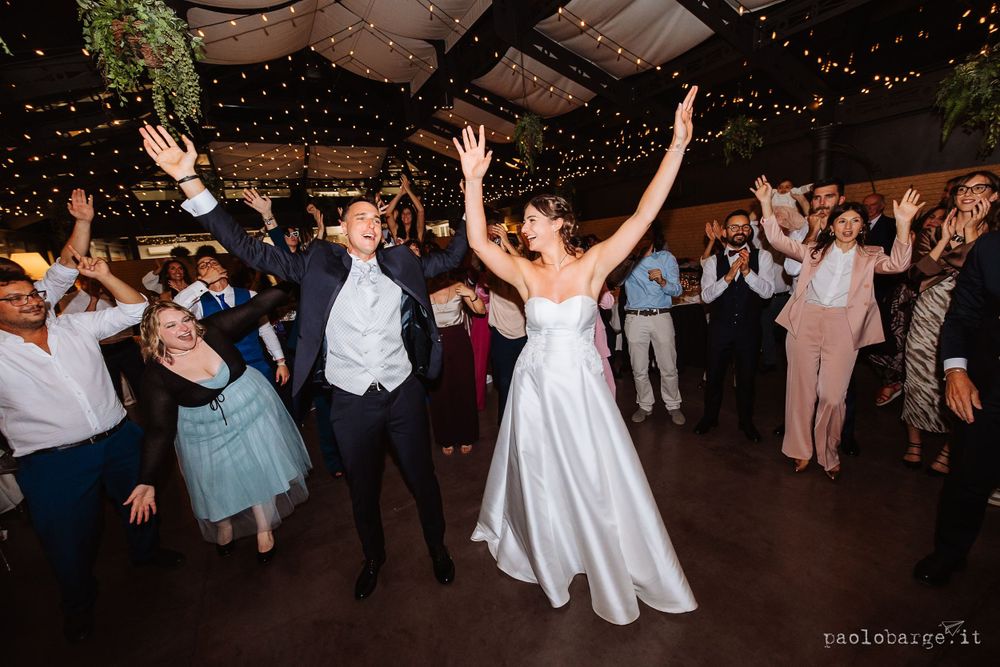 Wedding guests dancing and celebrating under a canopy of string lights at an indoor reception.