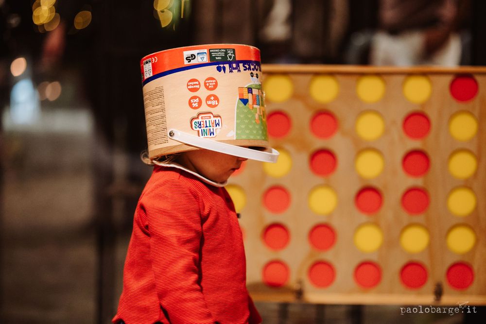 Creative portrait of person wearing a cereal box as mask next to a large Connect Four game.