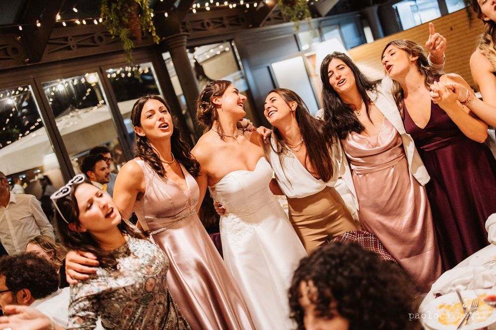 Wedding party celebrating and singing together at a reception under string lights.