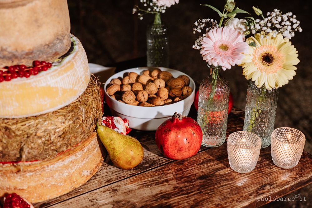Rustic wedding dessert table with tiered cake, gerbera daisies, and fresh fruit on wooden surface.