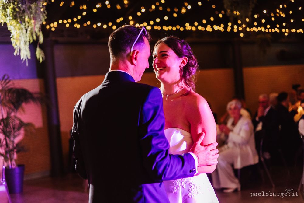 Romantic dance moment under purple lighting and string lights at wedding reception.